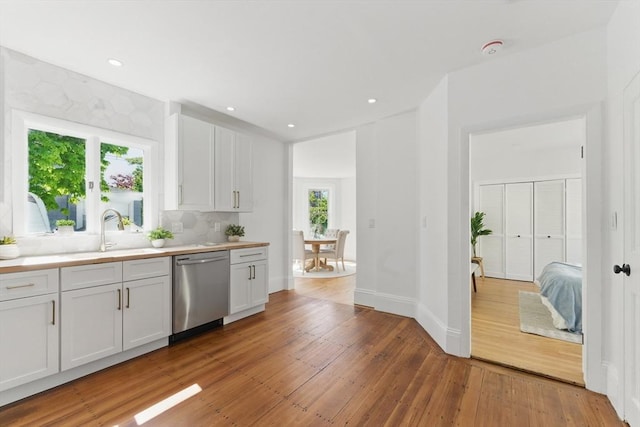 kitchen featuring stainless steel dishwasher, light wood-style floors, light countertops, a sink, and white cabinetry