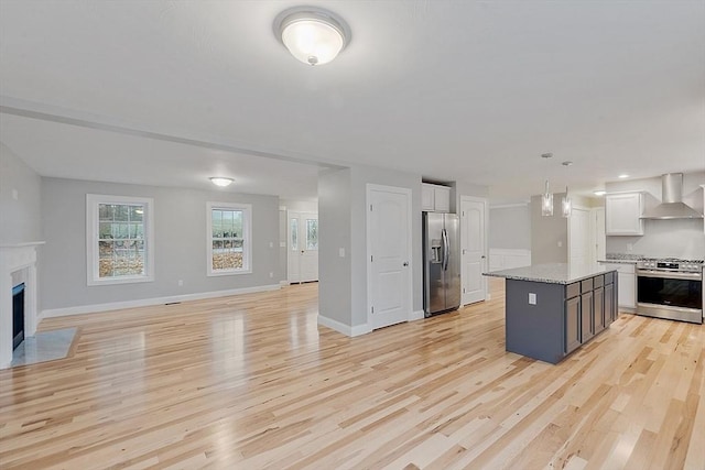 kitchen with appliances with stainless steel finishes, wall chimney range hood, light wood-style flooring, open floor plan, and white cabinetry
