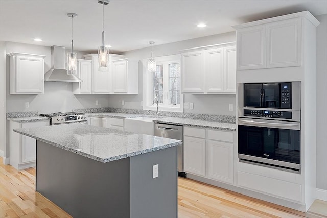 kitchen featuring stainless steel appliances, wall chimney exhaust hood, light wood finished floors, a sink, and recessed lighting