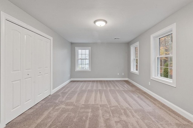 unfurnished bedroom with baseboards, light carpet, and a closet