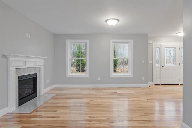 unfurnished living room with light wood finished floors, baseboards, and a high end fireplace