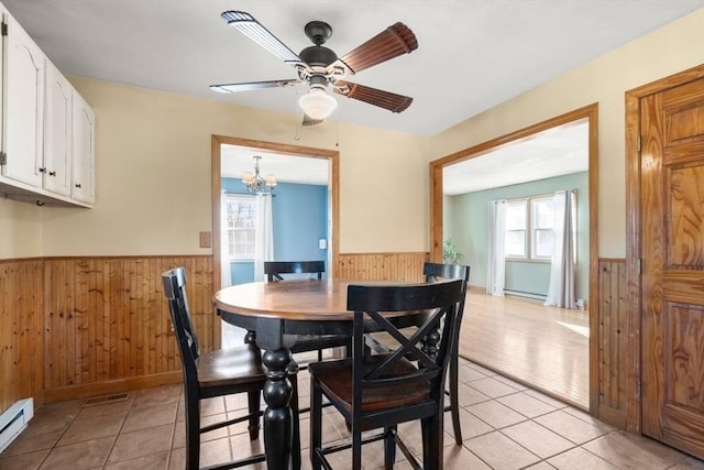 dining area featuring light tile patterned flooring, wooden walls, ceiling fan with notable chandelier, and a baseboard heating unit