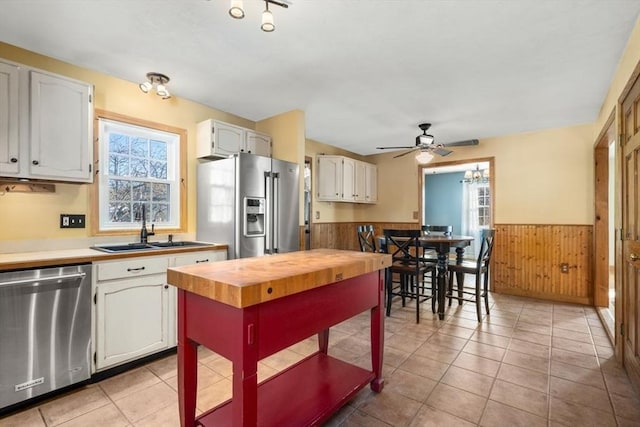 kitchen with white cabinetry, sink, wooden walls, and stainless steel appliances