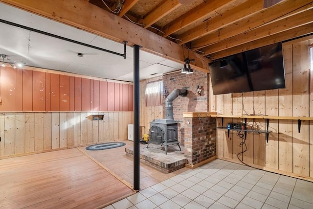 basement with wooden walls, light wood-type flooring, and a wood stove