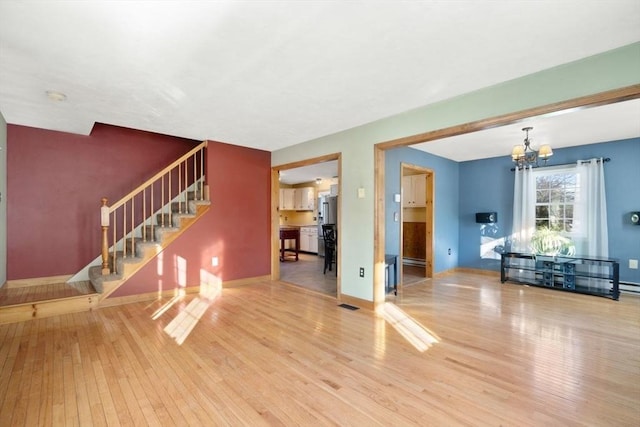 unfurnished living room featuring hardwood / wood-style flooring, a notable chandelier, and baseboard heating