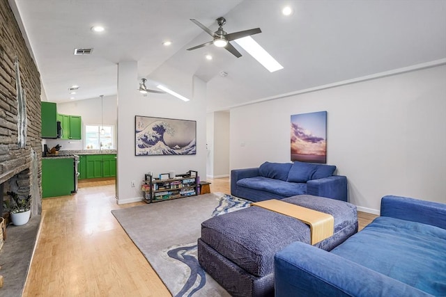 128 Clinton St, Hopkinton, MA 01748 - living room featuring ceiling fan, vaulted ceiling, light wood finished floors, a stone fireplace, and a skylight