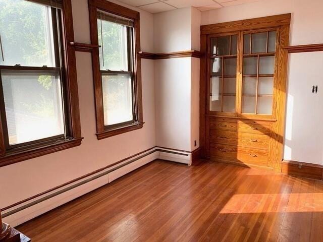 spare room with a paneled ceiling, a baseboard radiator, and light hardwood / wood-style flooring