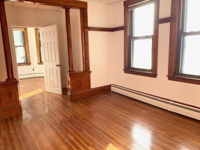 spare room featuring hardwood / wood-style flooring, ornate columns, and a baseboard radiator