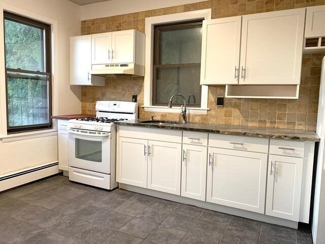 kitchen featuring dark stone counters, sink, decorative backsplash, white gas range, and white cabinetry