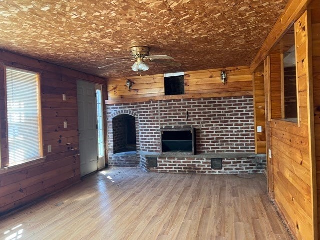 unfurnished living room with hardwood / wood-style flooring, ceiling fan, a fireplace, and wooden walls