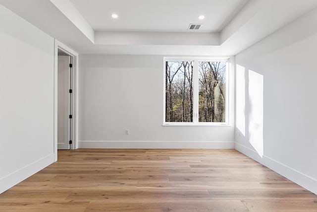 spare room with a tray ceiling and light hardwood / wood-style flooring