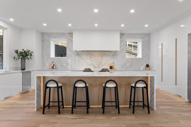 kitchen with a large island, light wood-type flooring, white cabinets, and a kitchen breakfast bar