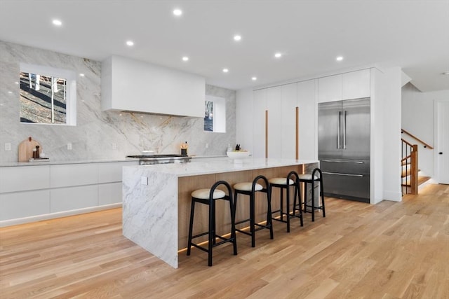 kitchen featuring a large island, stainless steel built in refrigerator, light stone countertops, a breakfast bar, and white cabinetry