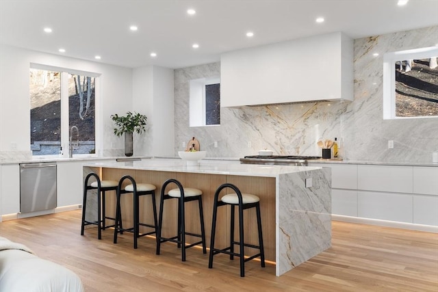 kitchen featuring light stone countertops, custom exhaust hood, a spacious island, a breakfast bar area, and white cabinets