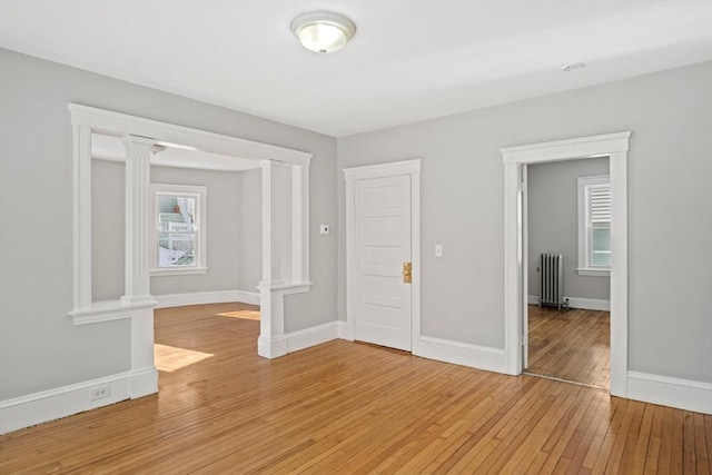 unfurnished room with hardwood / wood-style flooring, radiator, and ornate columns