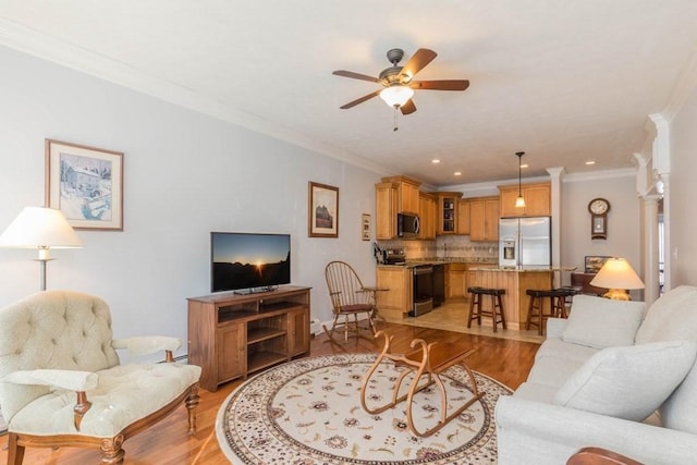 living room with crown molding, light hardwood / wood-style flooring, ceiling fan, and ornate columns