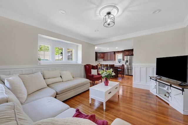 living room with crown molding, wainscoting, a healthy amount of sunlight, and light wood-type flooring