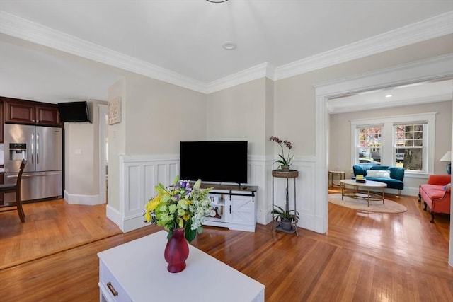 living area with crown molding, light wood finished floors, and a wainscoted wall