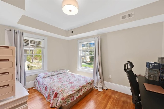 bedroom with baseboards, a tray ceiling, visible vents, and light wood-style flooring