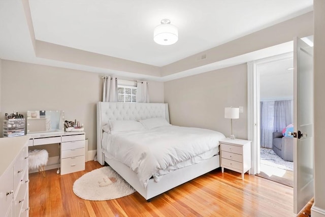 bedroom with a tray ceiling and light wood-style floors