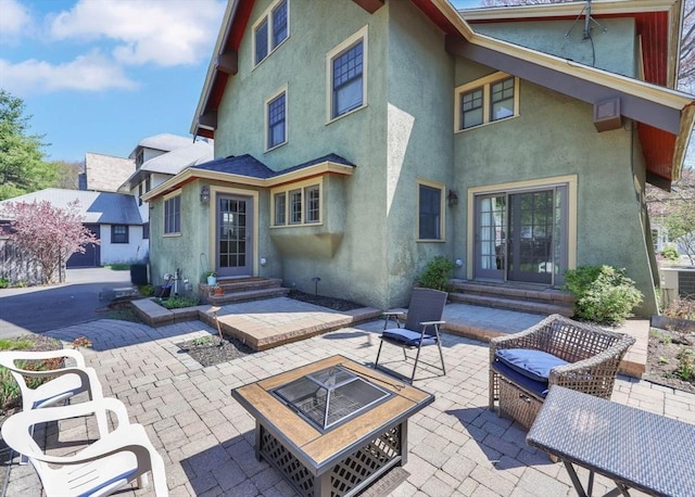 rear view of property featuring entry steps, a patio, stucco siding, and an outdoor fire pit