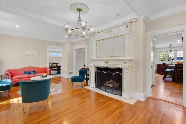 living area with crown molding, a notable chandelier, light wood-style floors, a fireplace with flush hearth, and visible vents