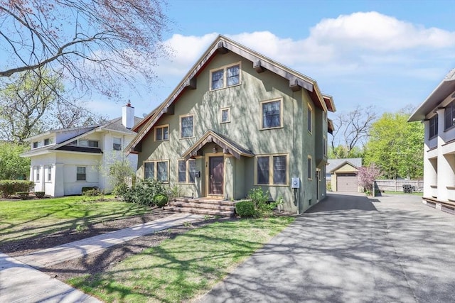 view of front of home featuring an outbuilding, a garage, aphalt driveway, a front lawn, and stucco siding