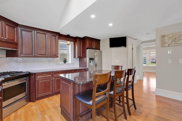 kitchen featuring light wood-style floors, decorative backsplash, appliances with stainless steel finishes, and a kitchen breakfast bar