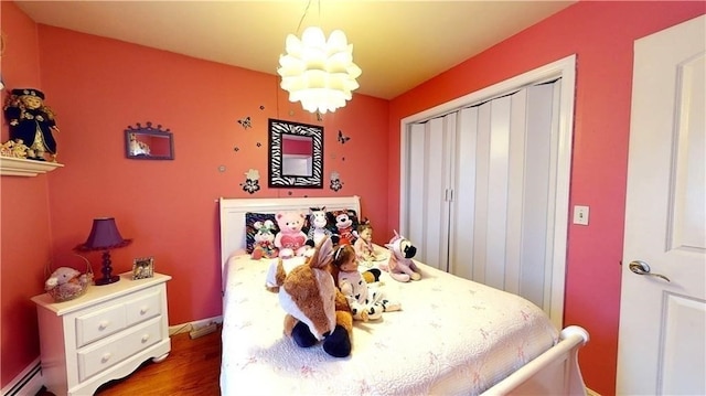 bedroom with hardwood / wood-style floors, a baseboard radiator, a closet, and a notable chandelier