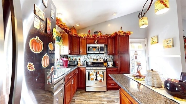 kitchen with backsplash, dark stone countertops, pendant lighting, vaulted ceiling, and appliances with stainless steel finishes