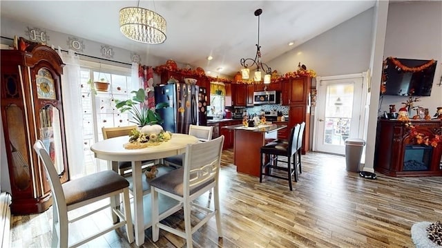 dining area featuring baseboard heating, high vaulted ceiling, light hardwood / wood-style floors, and a notable chandelier