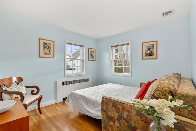 bedroom with radiator heating unit, baseboards, visible vents, and light wood-type flooring