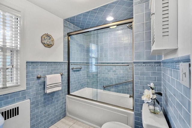 bathroom featuring shower / bath combination with glass door, radiator heating unit, tile patterned flooring, wainscoting, and tile walls