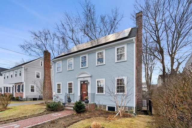 colonial house with roof mounted solar panels and a chimney