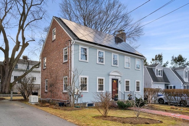 colonial home with roof mounted solar panels, a chimney, and a front lawn