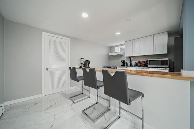 123 Walnut St, Saugus, MA 01906 - kitchen with stainless steel microwave, recessed lighting, white cabinets, wood counters, and a breakfast bar
