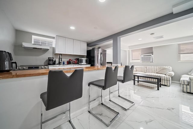 123 Walnut St, Saugus, MA 01906 - kitchen featuring butcher block counters, stainless steel appliances, a breakfast bar area, under cabinet range hood, and white cabinetry