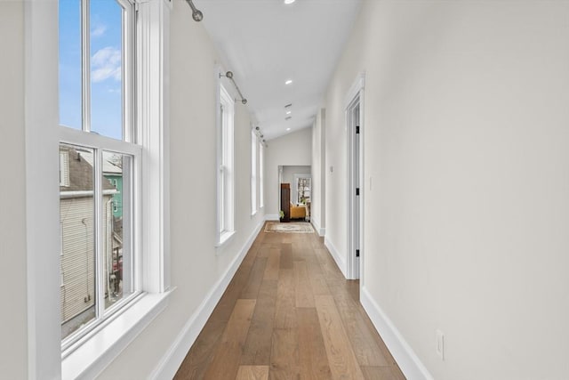 corridor featuring a barn door, baseboards, lofted ceiling, wood finished floors, and recessed lighting