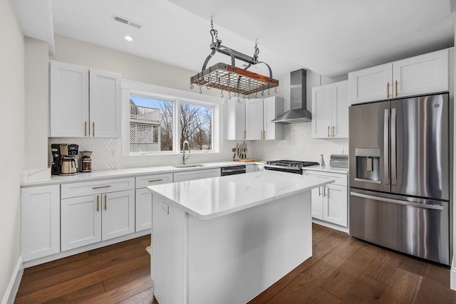 kitchen featuring visible vents, dark wood finished floors, appliances with stainless steel finishes, wall chimney range hood, and a sink