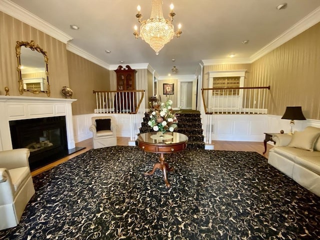 living room featuring a decorative wall, a wainscoted wall, stairs, a glass covered fireplace, and crown molding