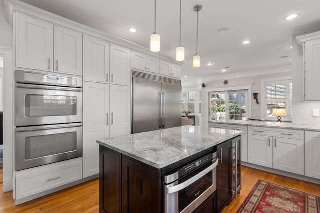 kitchen with white cabinetry, light wood finished floors, light stone countertops, and appliances with stainless steel finishes