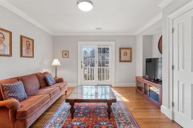 living area featuring visible vents, baseboards, ornamental molding, and light wood finished floors