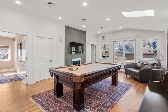 playroom with vaulted ceiling with skylight, light wood-style floors, visible vents, and a wealth of natural light