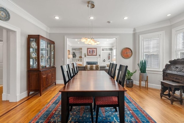 dining space with a fireplace, baseboards, light wood finished floors, and ornamental molding