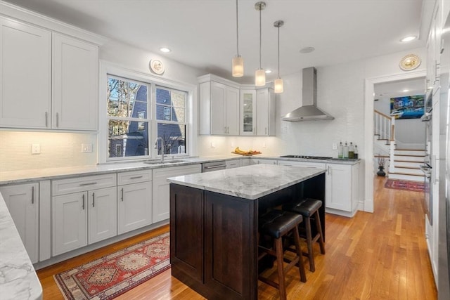 kitchen with light wood-type flooring, a sink, stovetop, wall chimney exhaust hood, and white cabinets