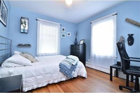 bedroom with a ceiling fan, wood finished floors, and baseboard heating
