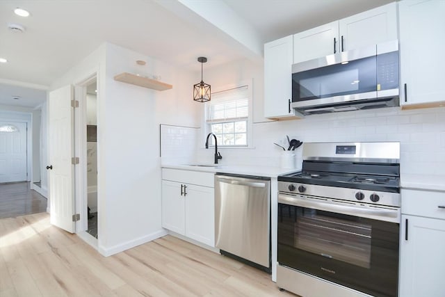 kitchen with white cabinets, stainless steel appliances, decorative light fixtures, and sink