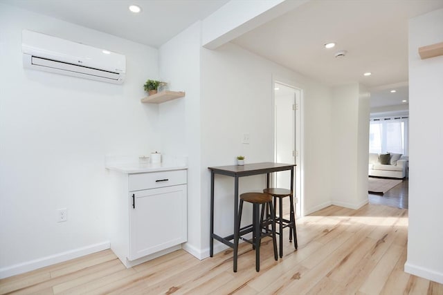 bar with an AC wall unit, light hardwood / wood-style floors, and white cabinets