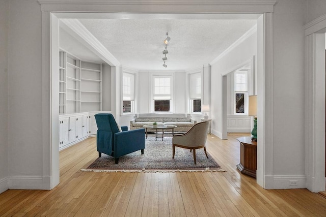 sitting room with ornamental molding, light wood-type flooring, a textured ceiling, and built in shelves