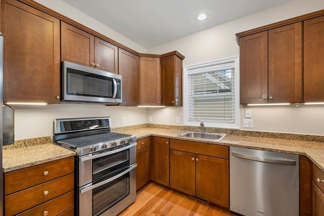 kitchen featuring light stone countertops, stainless steel appliances, light hardwood / wood-style flooring, and sink